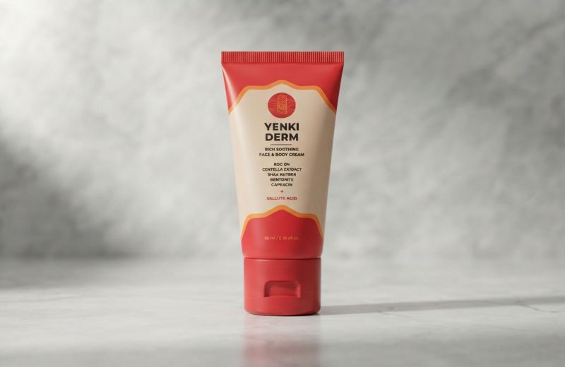 Yenki Derm Review: Un frasco de crema Yenki Derm rodeado de ingredientes naturales como cúrcuma y flores de manzanilla.